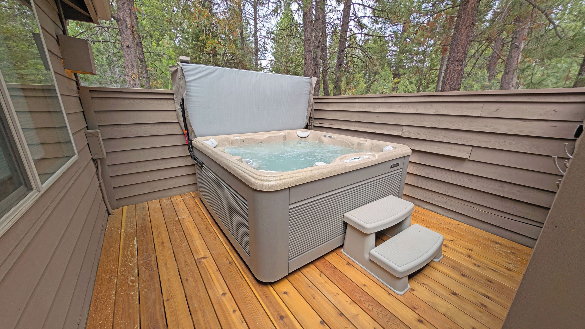 A hot tub on a wooden deck with a view of trees.