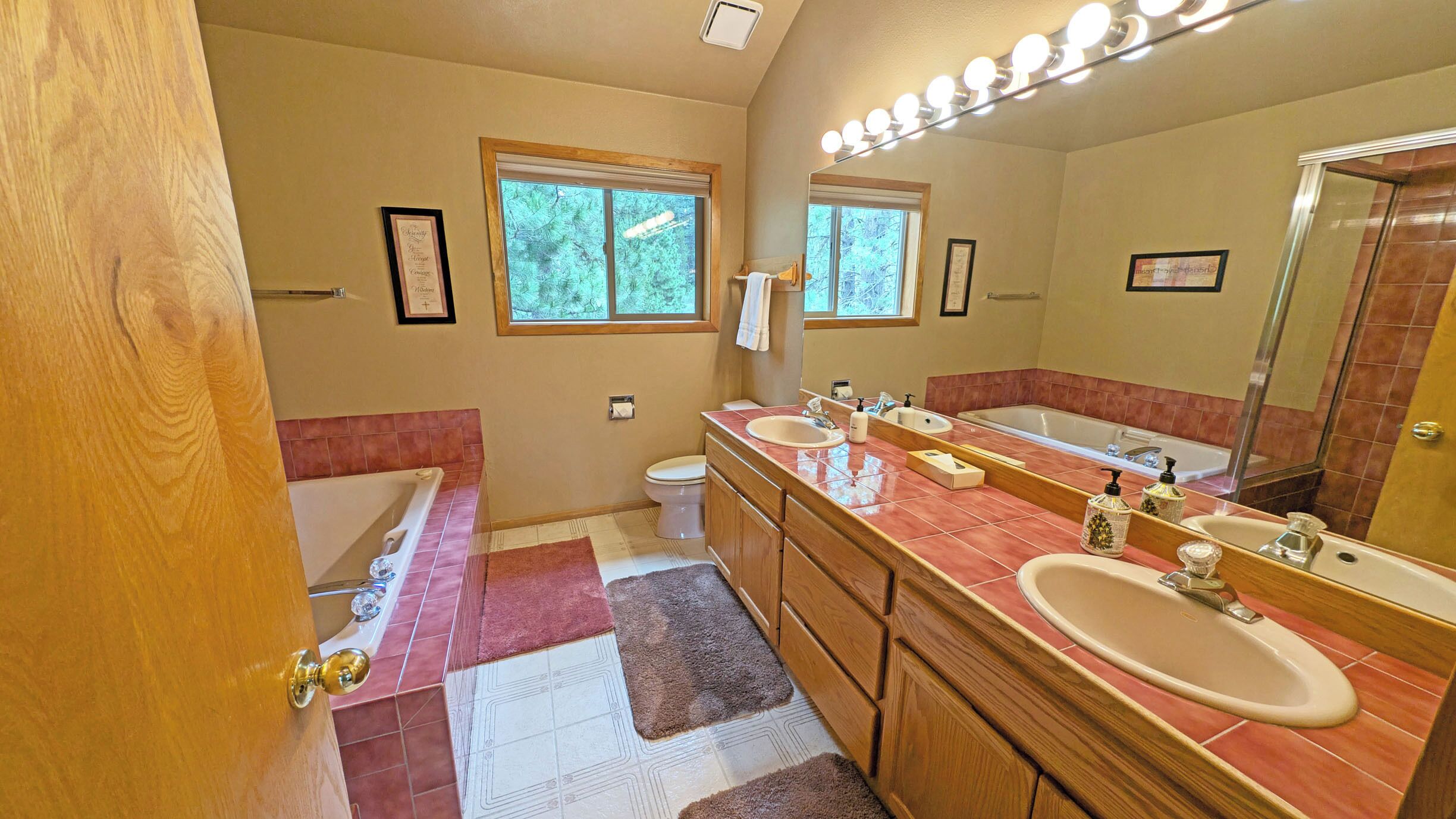 A bathroom with a bathtub, two sinks, a large mirror, and a window.