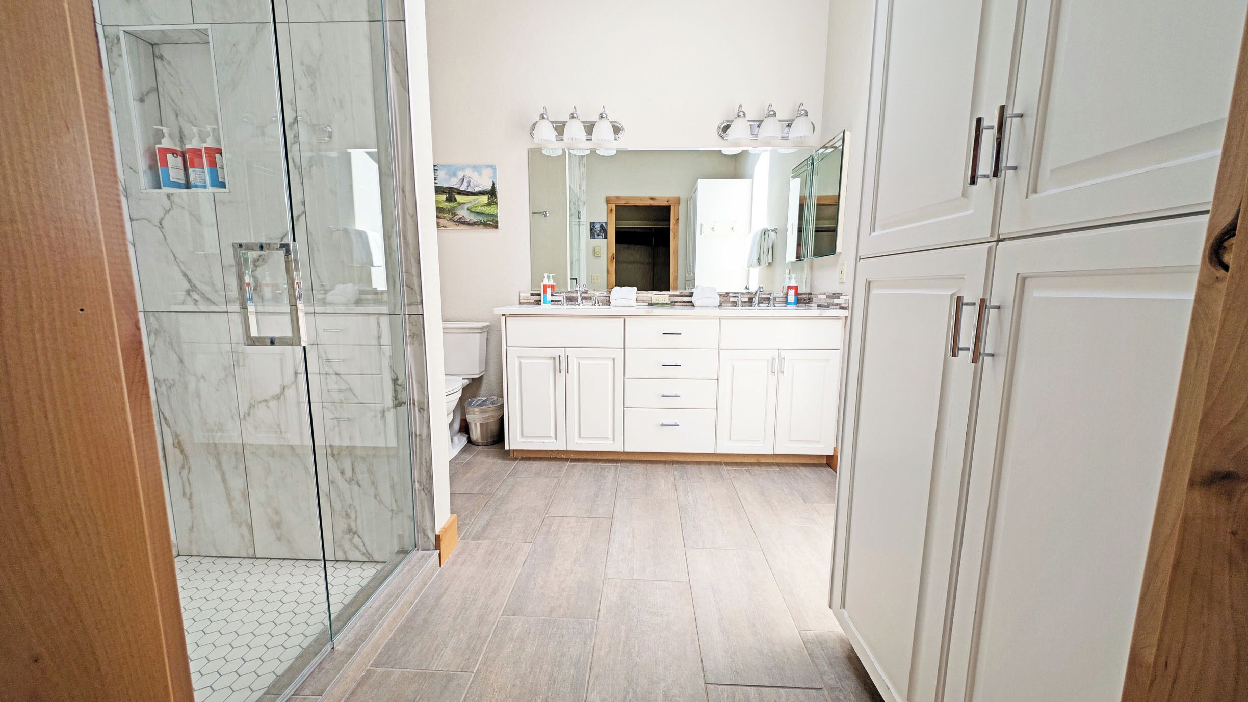 A modern bathroom with a glass shower enclosure, white cabinetry, and a large mirror.