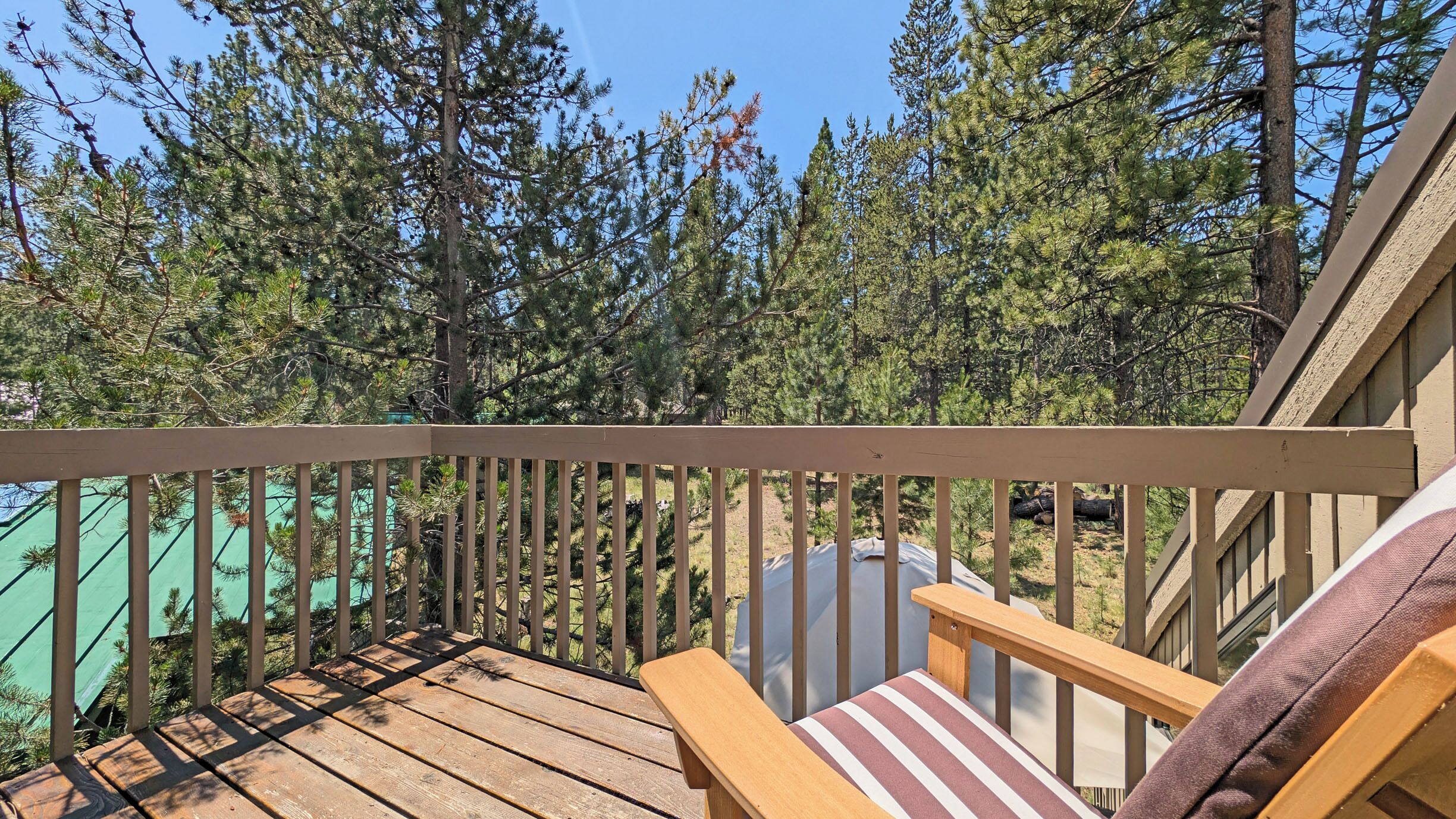 A wooden deck with a railing, a chair with a striped cushion, and a view of a forest of pine trees.