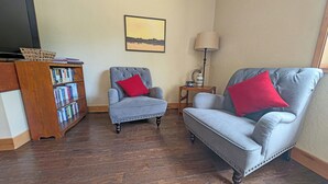 A living room with two grey armchairs, a wooden bookshelf, a framed picture on the wall, and a lamp on a side table. - East Butte 14 (Bend)