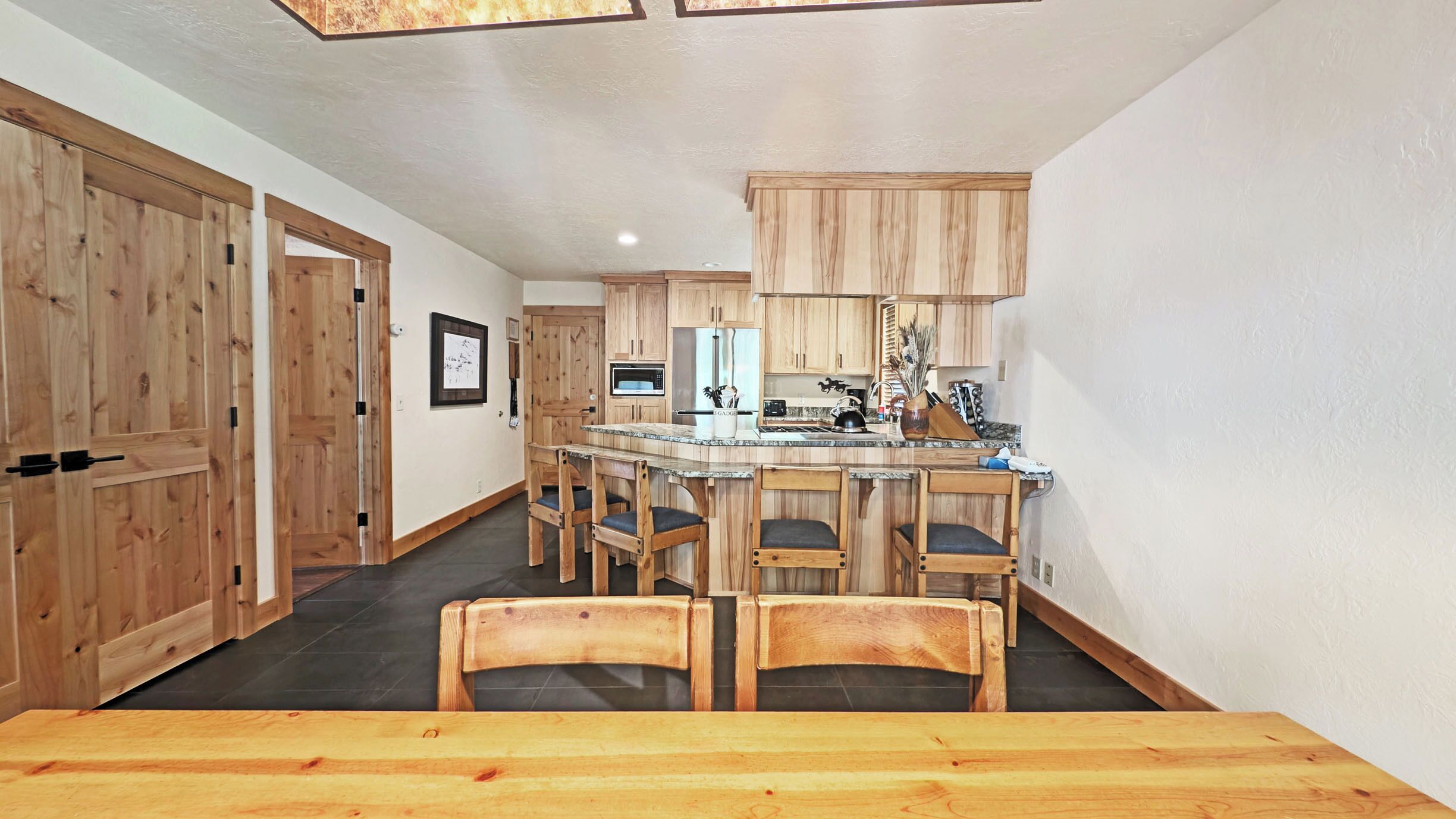 Una cocina moderna con armarios de madera, una isla central con taburetes y un comedor con mesa de madera.