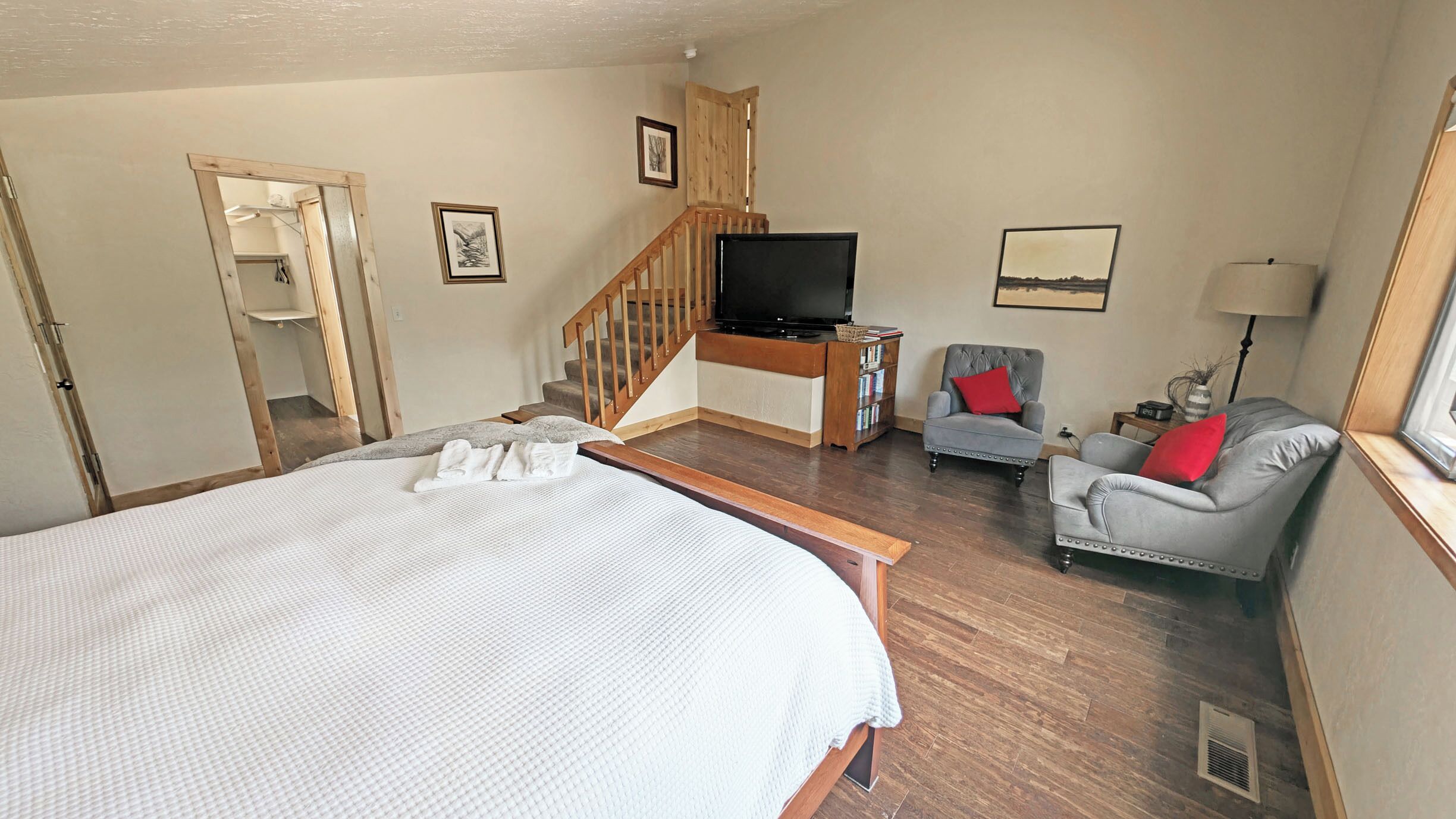 Une chambre d’hôtel avec un grand lit, une télévision, un fauteuil gris et un escalier.