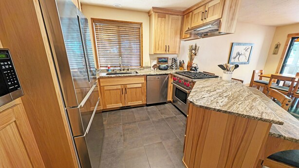 A kitchen with wooden cabinets, stainless steel appliances, a granite countertop, and a dining area with wooden chairs. - East Butte 14 (Bend)