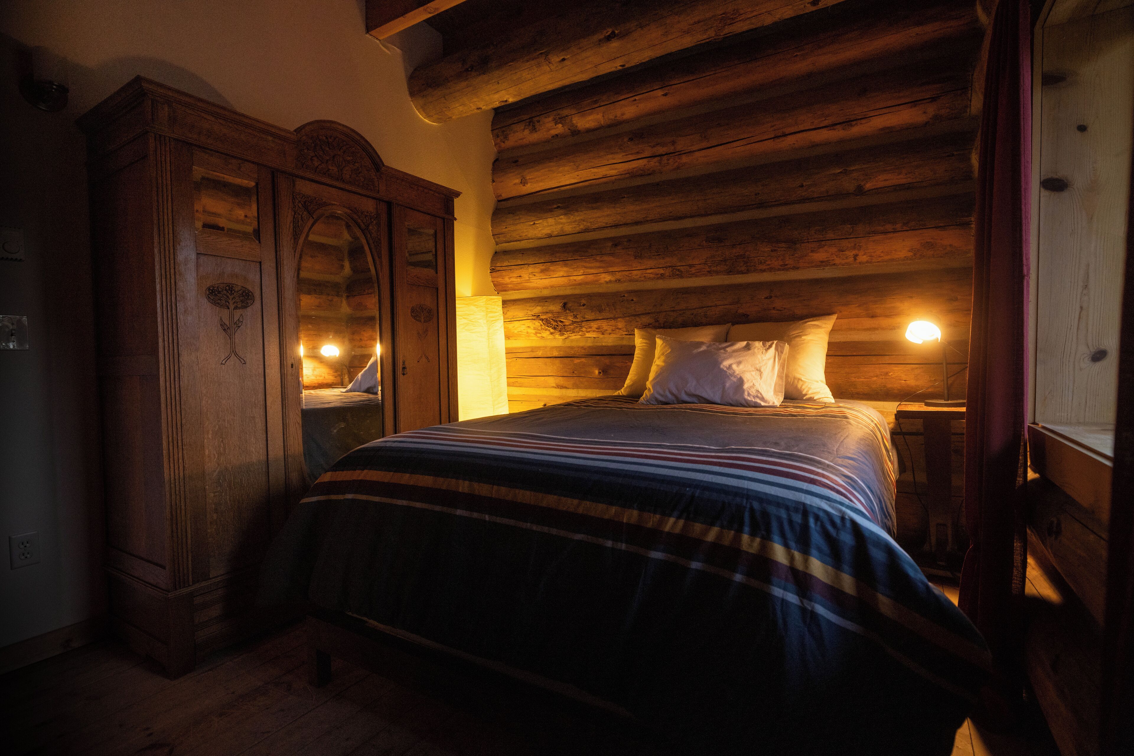 A wooden cabin-style bedroom with a bed, a nightstand, and a wardrobe.