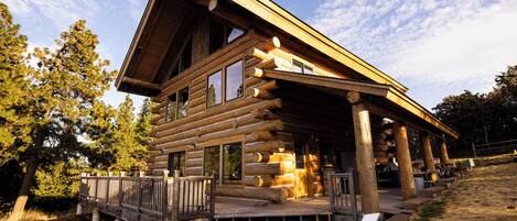 A log cabin with a porch, large windows, and a wooden deck.