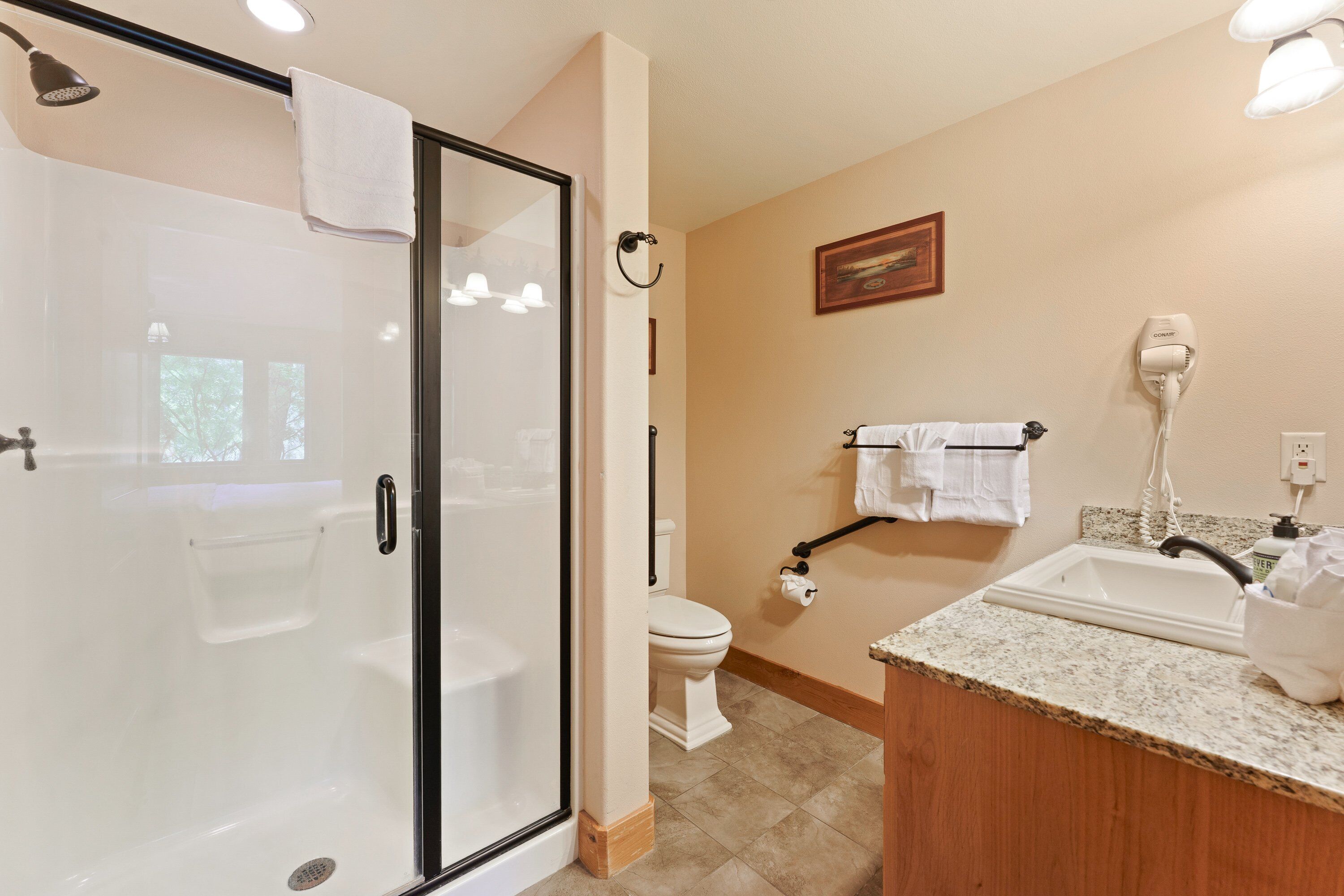 A modern bathroom with a glass shower enclosure, a toilet, a sink with a vanity, and a hairdryer on the wall.