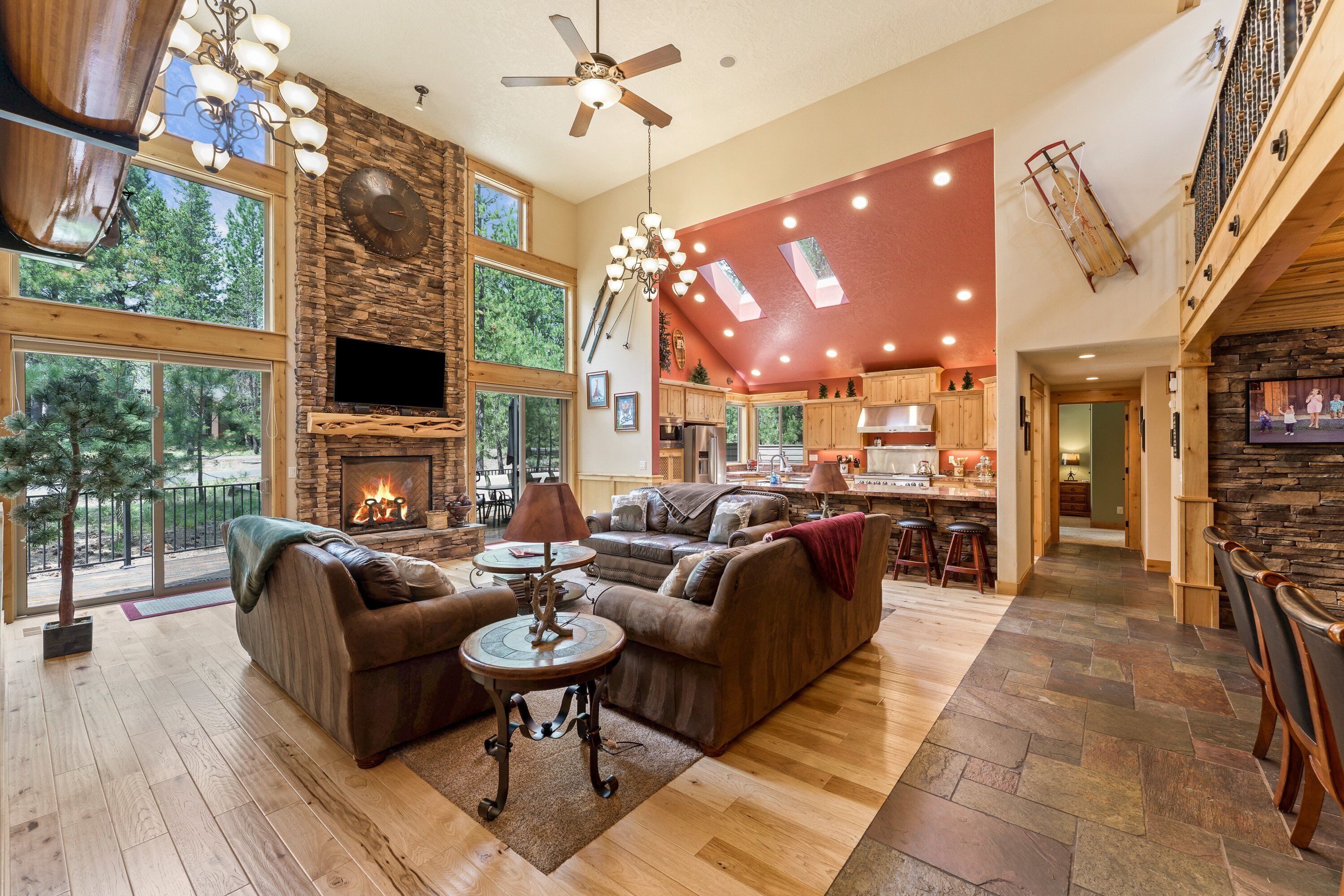 A spacious living room with a fireplace, large windows, and a high ceiling fan.