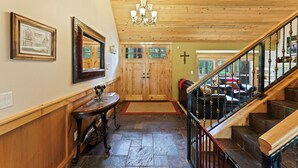 Eine Holztreppe mit schwarzer Geländer führt zu einer zweiten Etage. Im Hintergrund ist eine Holztür mit Glasfeldern zu sehen.