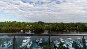 Ein Yachthafen mit vertäuten Booten, ein Fluss im Hintergrund und bewaldete Ufer auf der anderen Seite des Wassers.