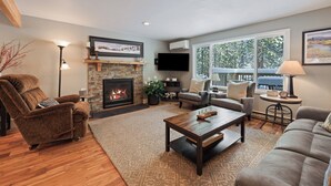 A living room with a fireplace, a sofa, a coffee table, and a TV mounted on the wall. - Sunriver Hot Tub Home With Sharc Passes (Bend)