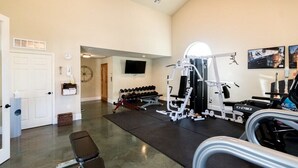 A gym with exercise equipment, a bench, dumbbells, and a television on the wall. - Stateroom Elite (Merritt Island)
