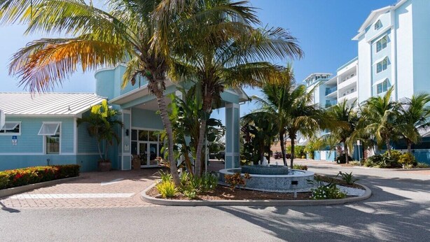 A hotel entrance with a covered walkway, palm trees, and a central fountain. - Stateroom Elite (Merritt Island)