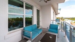 A balcony with a sofa and chairs, large windows, and a view of a river and greenery. - Stateroom Elite (Merritt Island)