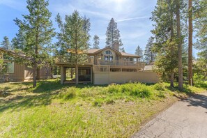 A two-story house with a covered porch, surrounded by tall pine trees. - Sunriver Golf Views Hot Tub Escape (Bend)