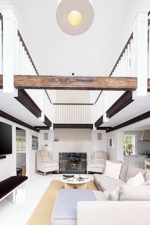A spacious living room with a high ceiling, a large flat-screen TV, and a staircase leading to an upper level. - Bridgehaven Estate by Rove - Luxe Home With Pool (Bridgehampton)