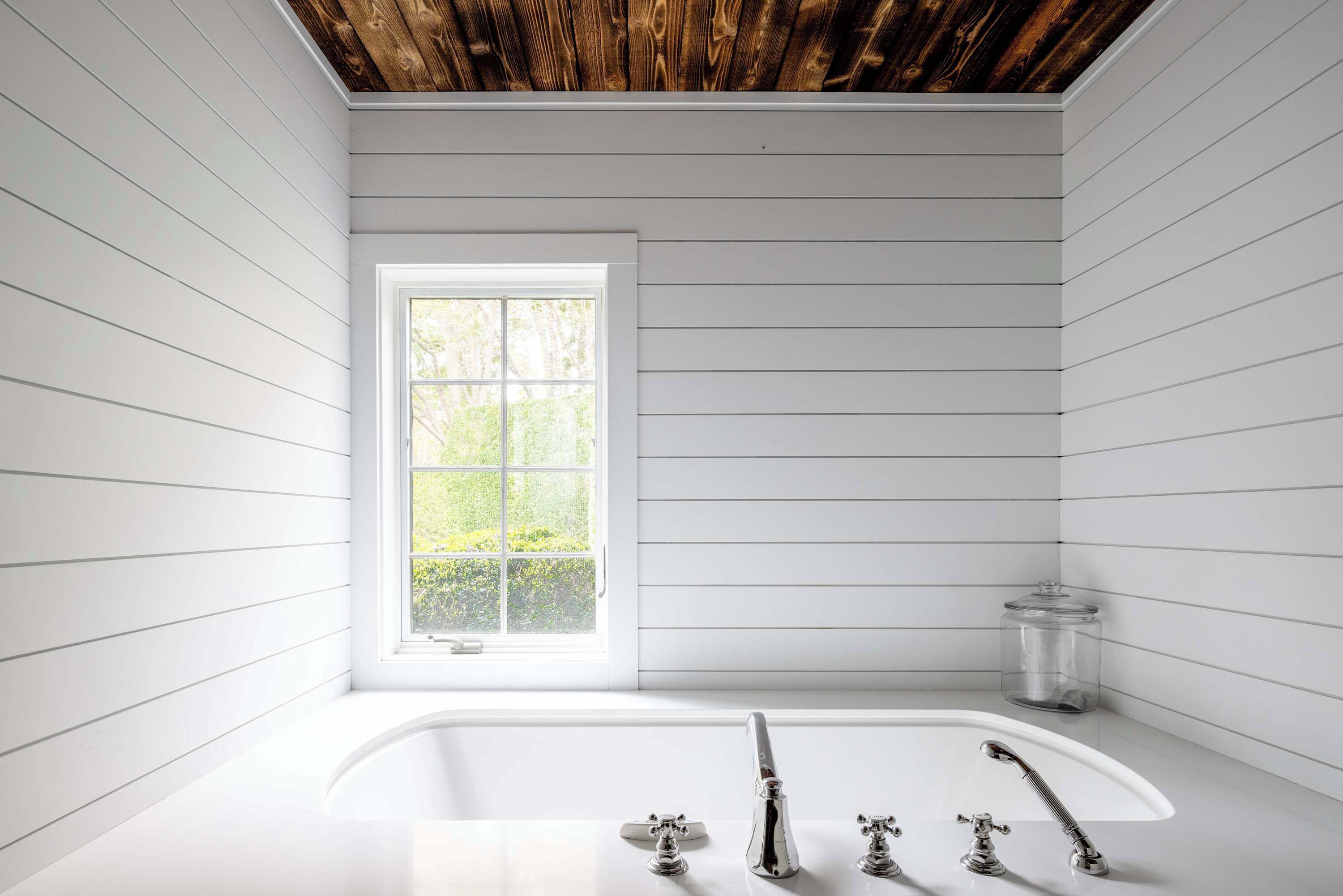 Une salle de bain avec une baignoire blanche, une fenêtre donnant sur un paysage verdoyant et un plafond en bois.