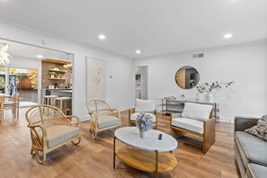 A modern living room with wicker furniture, a round coffee table, and a dining area with a wooden table and chairs. - Marbella Lane - Modern 3broasis in Siliconvalley (San Jose)