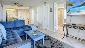 A living room with a sectional sofa, a coffee table, a TV, and a kitchen in the background. - Oceania Beach Club 203 (New Smyrna Beach)