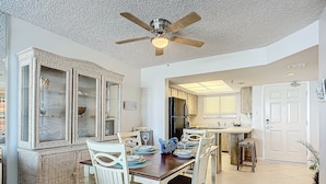 A dining area with a large mirror, a ceiling fan, and a kitchen in the background. - Oceania Beach Club 203 (New Smyrna Beach)