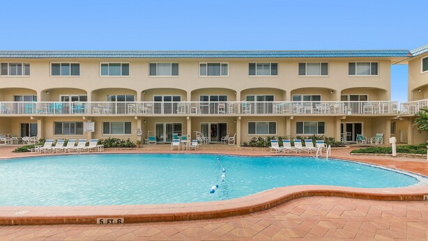 A hotel with a swimming pool, multiple balconies, and outdoor seating areas. - Win-san C102 (New Smyrna Beach)