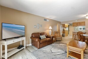 Ein Wohnzimmer mit Fernseher, Ledersofa und einem Essbereich mit Tisch und Stühlen.