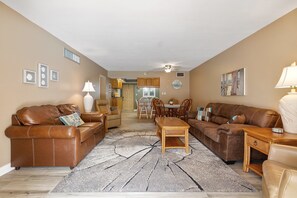 Ein Wohnzimmer mit zwei braunen Ledersofas, einem Holztisch und einem Essbereich mit Tisch und Stühlen.