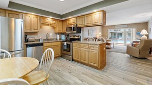A modern kitchen with wooden cabinets, stainless steel appliances, and a dining area with a table and chairs. - Win-san C102 (New Smyrna Beach)