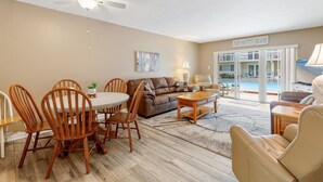 A spacious living room with a dining area, a brown leather sofa, wooden chairs, and a ceiling fan. - Win-san C102 (New Smyrna Beach)