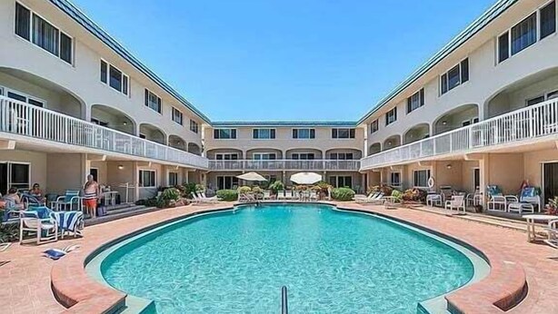 A pool area with a central pool, lounge chairs, and a multi-level building with balconies. - Win-san A212 (New Smyrna Beach)