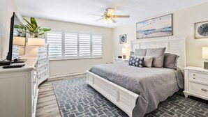 A bedroom with a bed, a ceiling fan, a window with blinds, a bedside table with a lamp, and a dresser. - Win-san A212 (New Smyrna Beach)