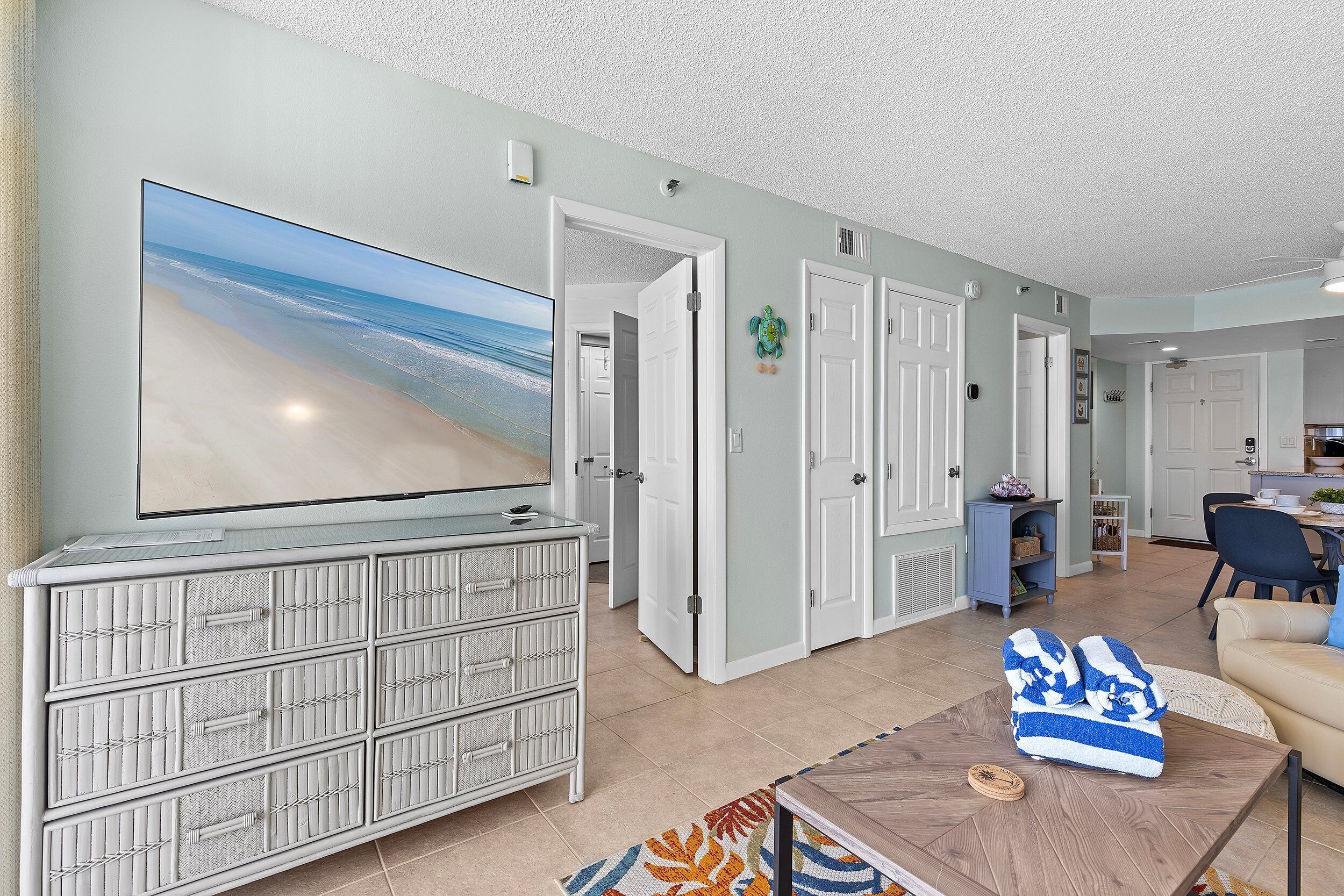 A living room with a large flat-screen TV, a white storage unit, a coffee table, and a beige sofa.