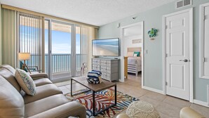 A living room with a sofa, a coffee table, and a view of the ocean through large windows. - Oceania Beach Club 704 (New Smyrna Beach)