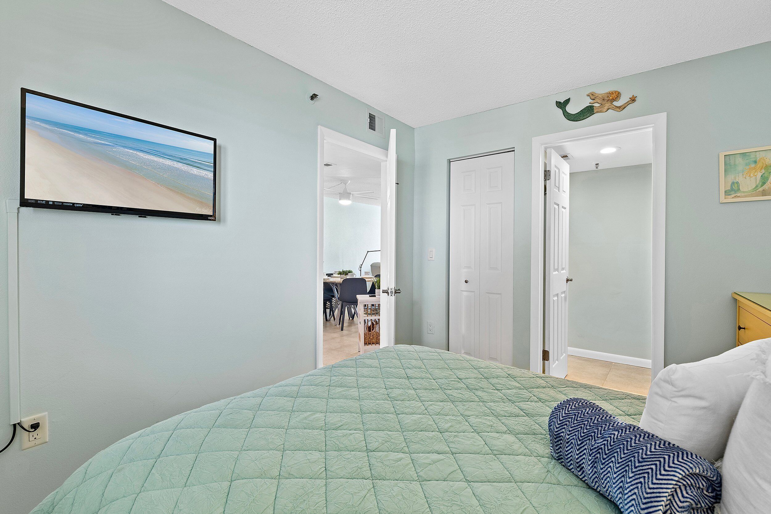 A bedroom with a bed, a television on the wall, and a door leading to another room.