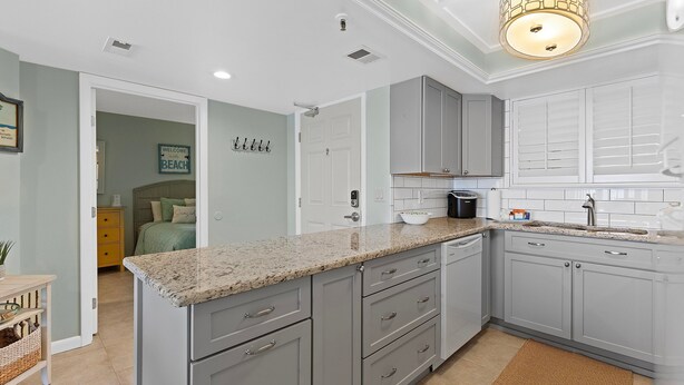 A modern kitchen with grey cabinets, a granite countertop, and a built-in dishwasher. - Oceania Beach Club 704 (New Smyrna Beach)