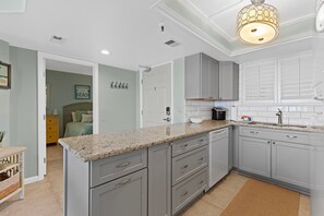 A modern kitchen with grey cabinets, a granite countertop, and a built-in dishwasher. - Oceania Beach Club 704 (New Smyrna Beach)