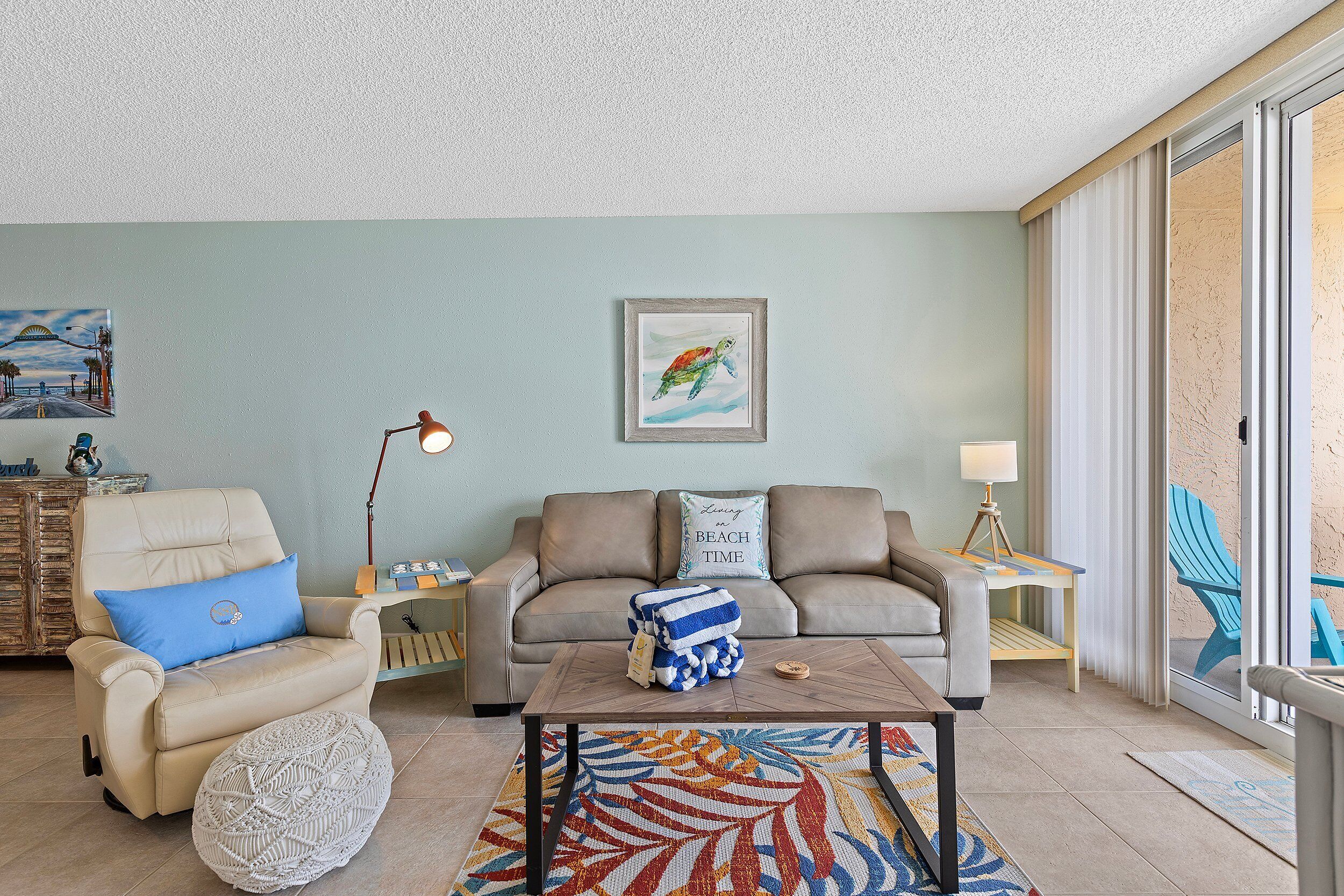 A living room with a beige sofa, a blue armchair, a coffee table, and a framed picture of a turtle.
