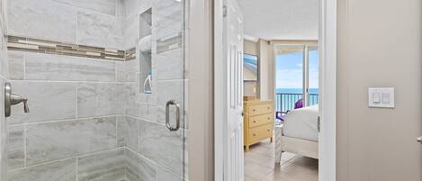 A bathroom with a shower, a toilet, and a sink. There is a door leading to a balcony with a view of the ocean.