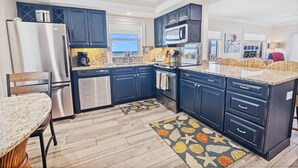 Μια μοντέρνα κουζίνα με σκούρα μπλε ντουλάπια, συσκευές από ανοξείδωτο ατσάλι και πάγκο από γρανίτη.