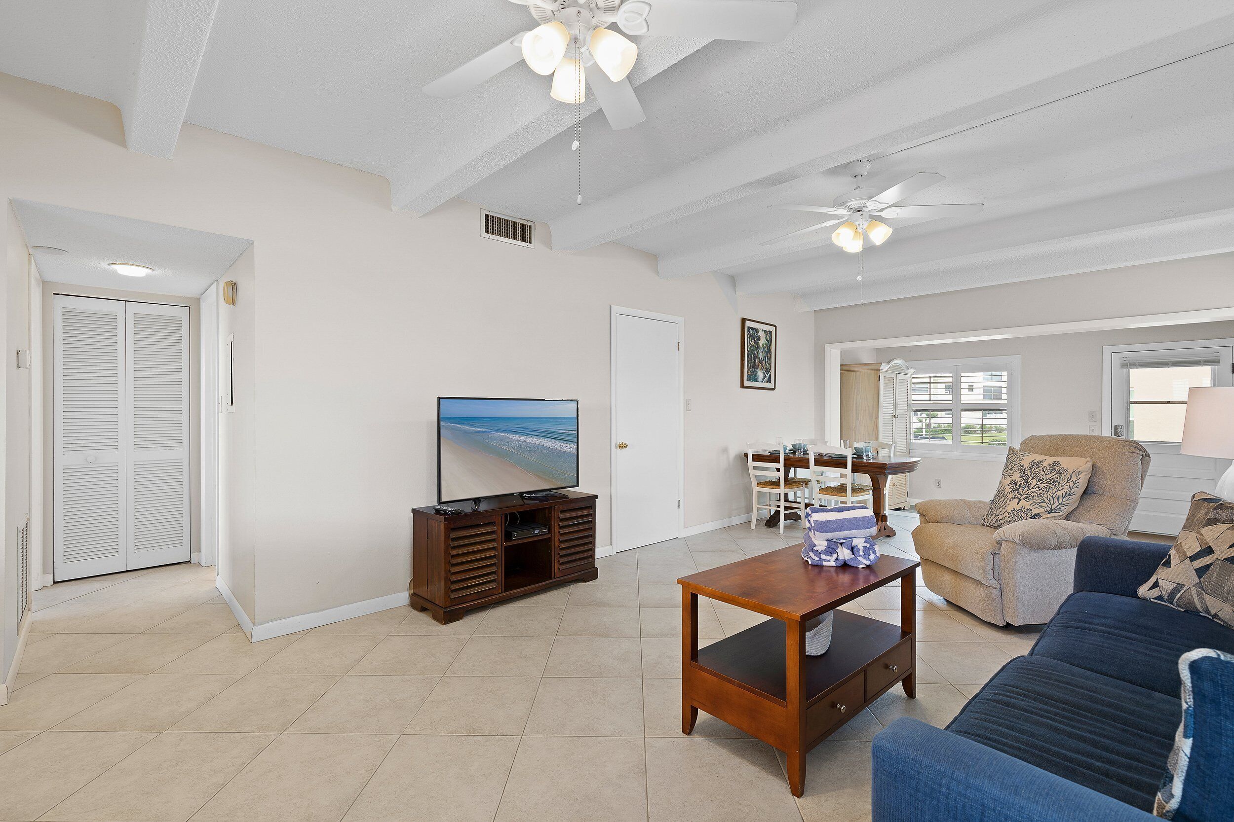 A spacious living room with a television, a sofa, a coffee table, and a ceiling fan.