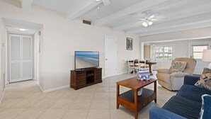 A spacious living room with a television, a sofa, a coffee table, and a ceiling fan. - Ocean Club North C104 (New Smyrna Beach)