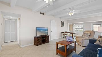 A spacious living room with a television, a sofa, a coffee table, and a ceiling fan.