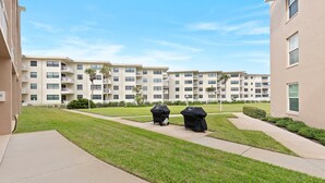 A residential building with multiple balconies, a well-maintained lawn, and a clear sky. - Ocean Club North C104 (New Smyrna Beach)