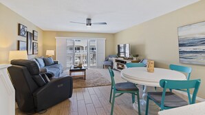 Ein Wohnzimmer mit schwarzem Sofa, Türkis-farbenen Sesseln, einem weißen Tisch und einem Deckenventilator.