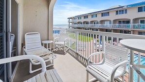 Ein Balkon mit weißen Stühlen und einem Tisch, der auf einen Pool und ein Gebäude mit mehreren Balkonen blickt.