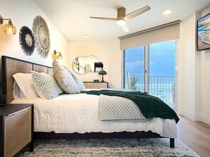 A bedroom with a large bed, a ceiling fan, a view of the ocean through a large window, and a balcony. - Oceania Beach Club 201 (New Smyrna Beach)