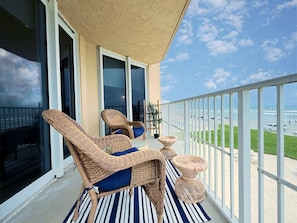 A balcony with wicker furniture, a striped rug, and a view of the beach. - Oceania Beach Club 201 (New Smyrna Beach)