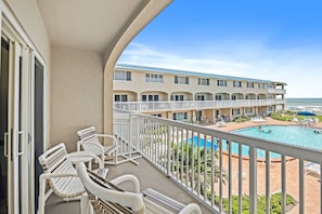 A balcony with white chairs, a pool, and a building with multiple balconies and windows. - Win-san B203 (New Smyrna Beach)