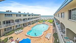A hotel with a swimming pool, lounge chairs, and a view of the ocean.