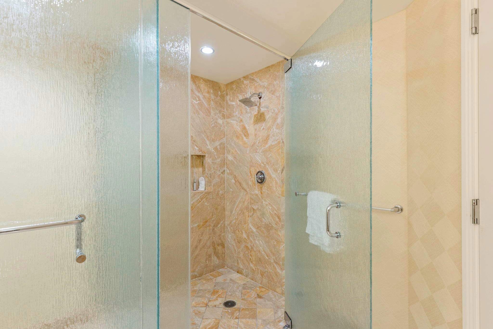 A glass-enclosed shower with a marble wall and a tiled floor.